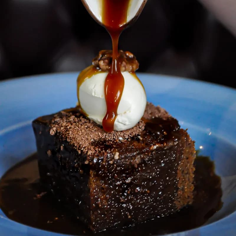 Sticky toffee pudding with caramel sauce poured over a scoop of ice cream